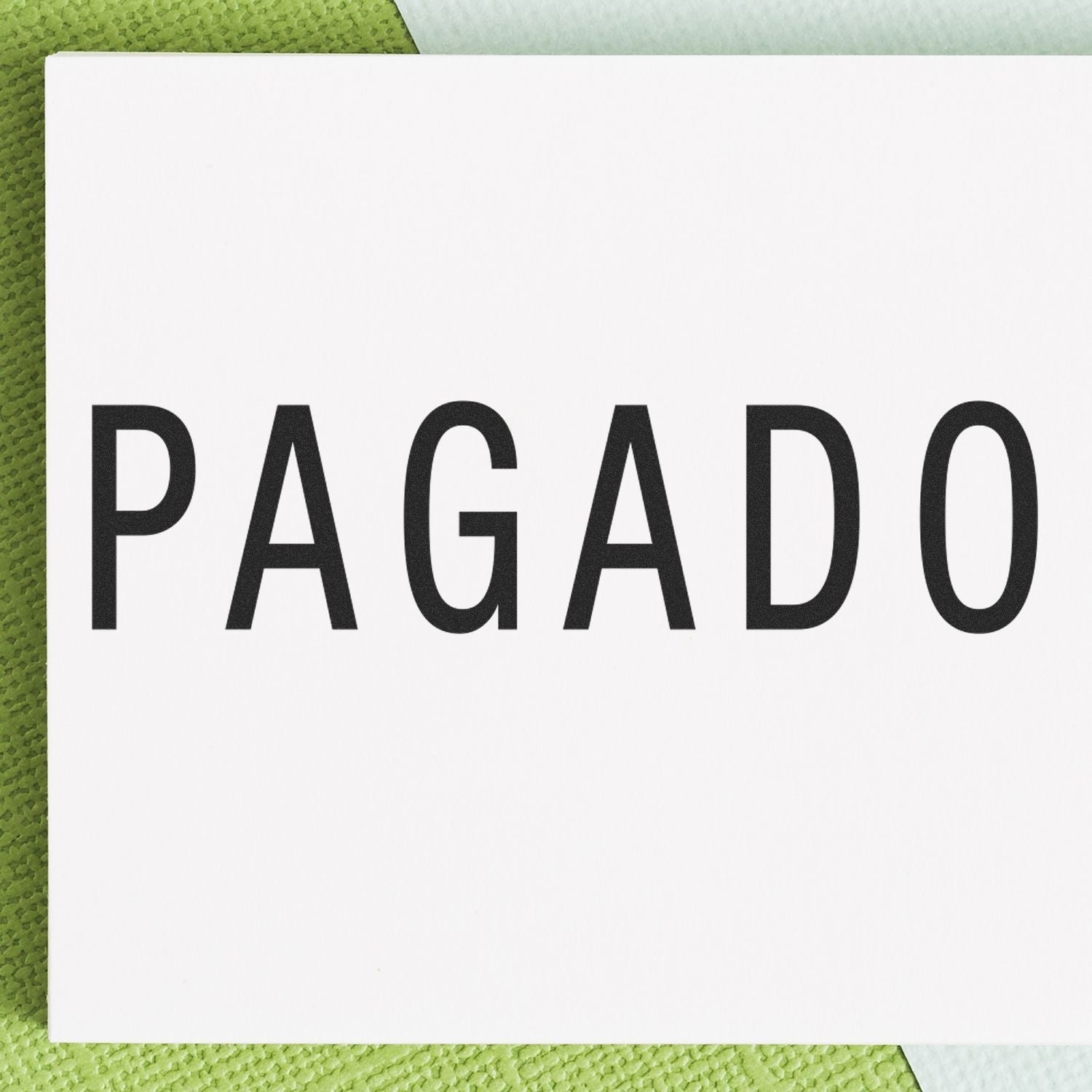 Close-up of a white paper stamped with the word 'PAGADO' using a Self Inking Pagado Stamp, placed on a green textured surface.