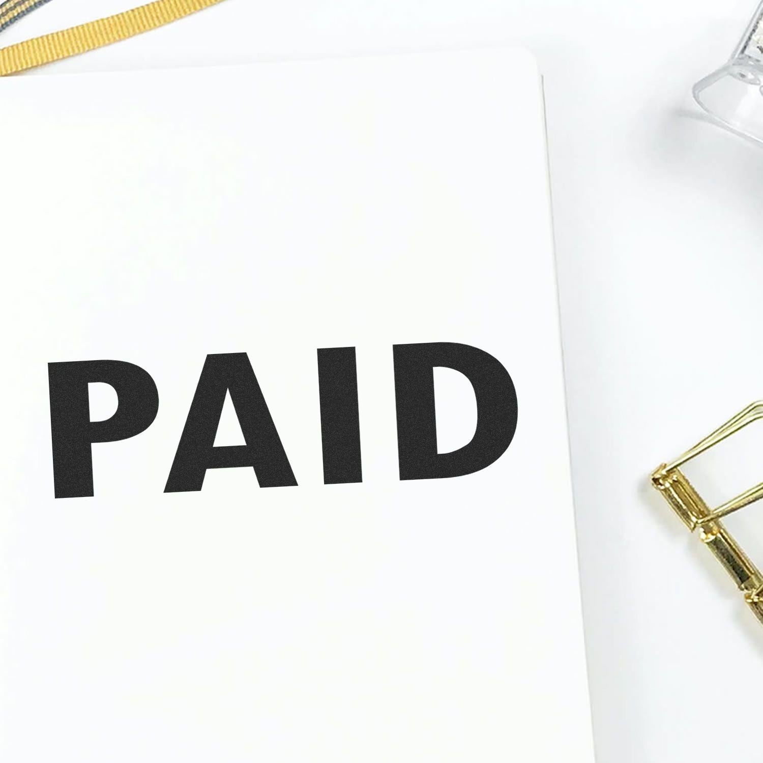 Self Inking Paid Stamp marking PAID in bold black letters on a white paper, with a gold paper clip and clear stamp holder nearby.