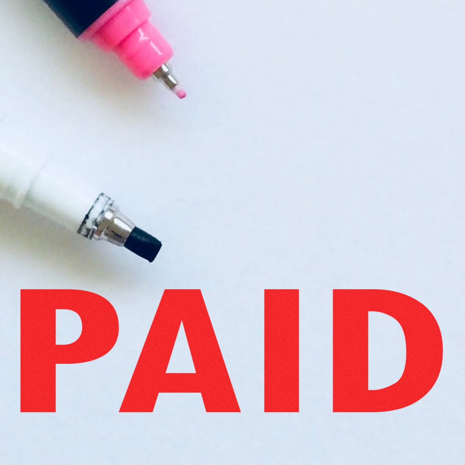 Close-up of a red 'PAID' rubber stamp mark with two marker pens, one pink and one white, on a white background.