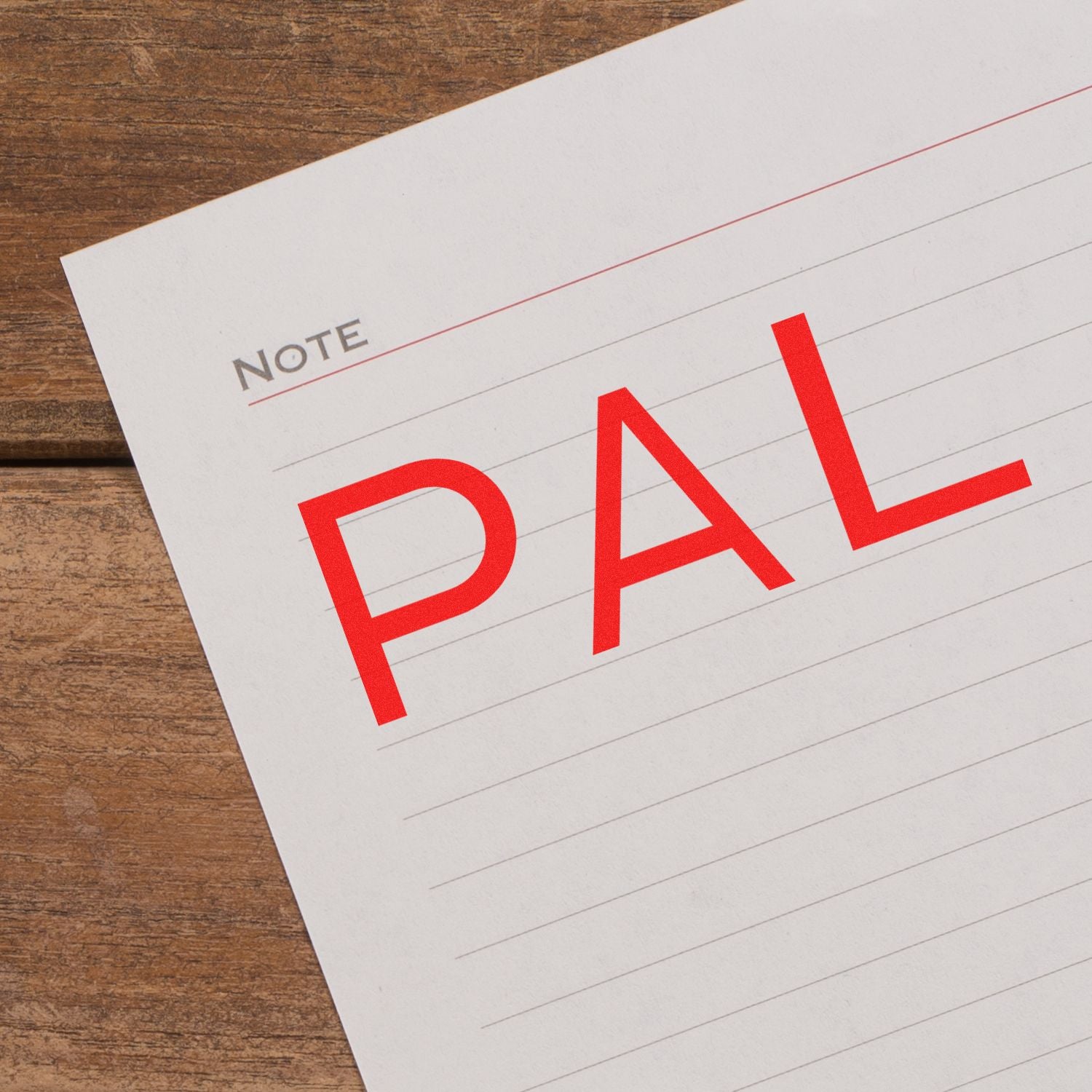 Note paper stamped with PAL in red ink using a Slim Pre-Inked PAL Stamp, placed on a wooden surface.