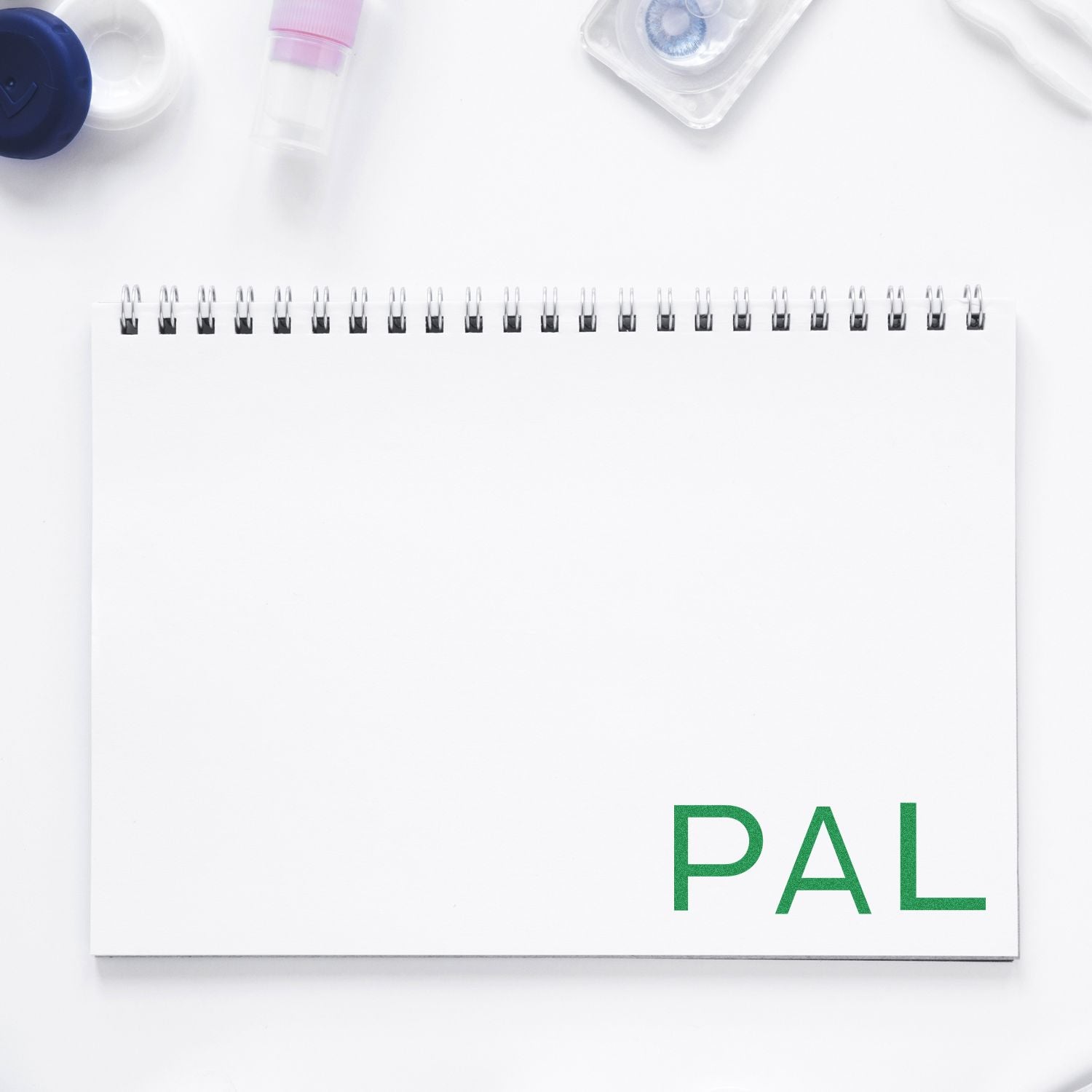 Large PAL Rubber Stamp in green ink on a white spiral notebook, surrounded by various office supplies on a white background.