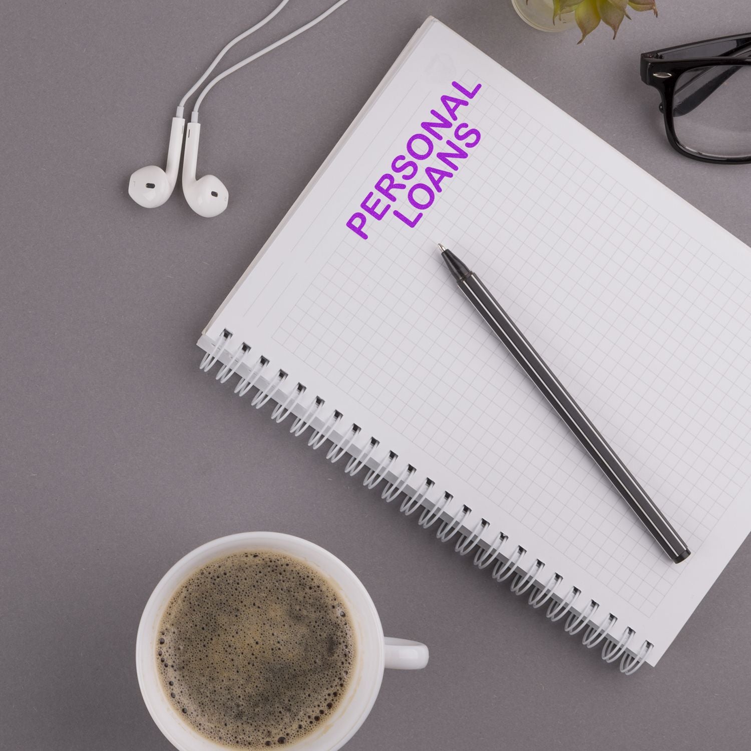 Notebook stamped with PERSONAL LOANS using the Large Personal Loans Rubber Stamp, alongside a pen, coffee cup, glasses, and earphones.