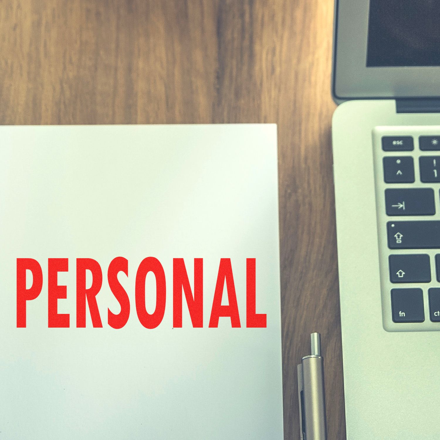 Self Inking Personal Stamp marking PERSONAL in red on paper, next to a laptop and pen on a wooden desk.