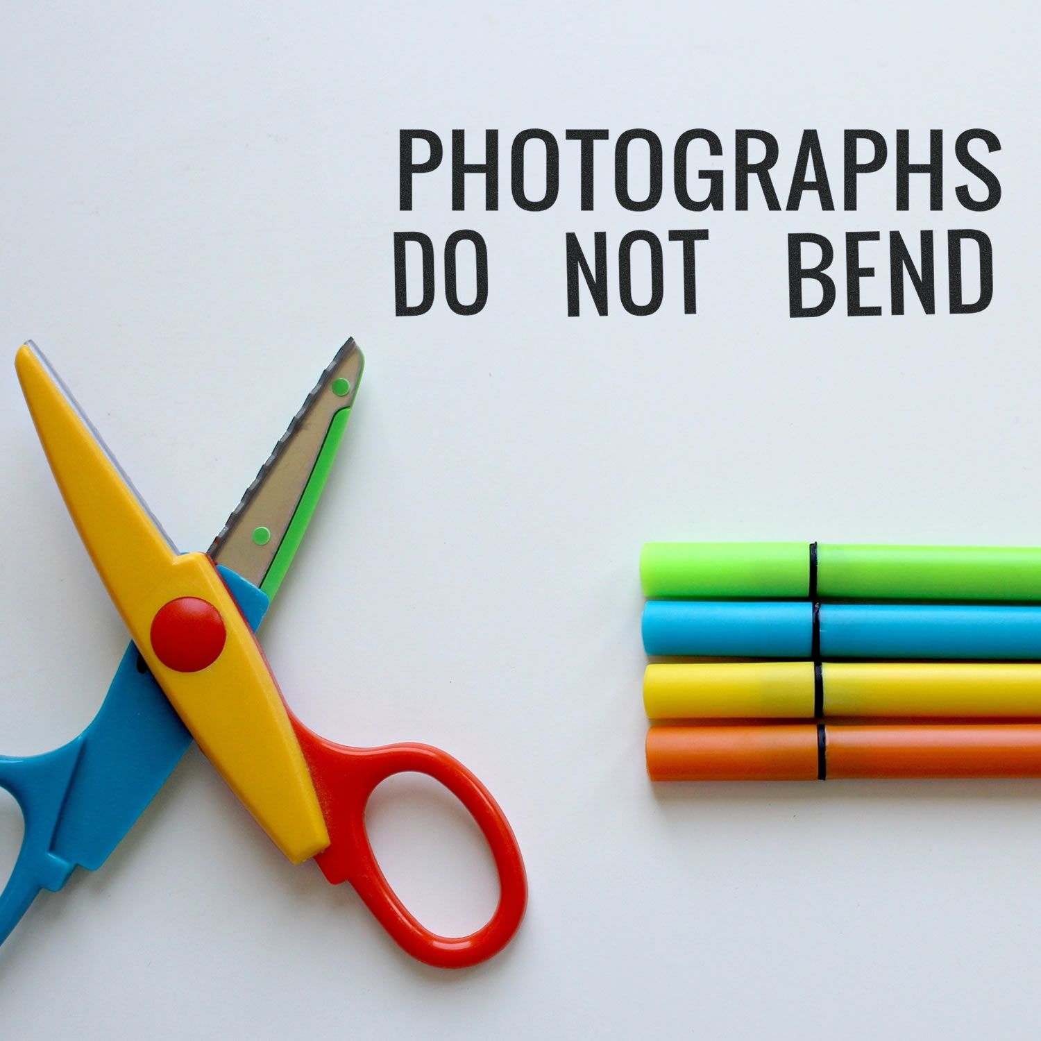 Self Inking Photographs Do Not Bend Stamp used on white paper with colorful scissors and markers beside it.