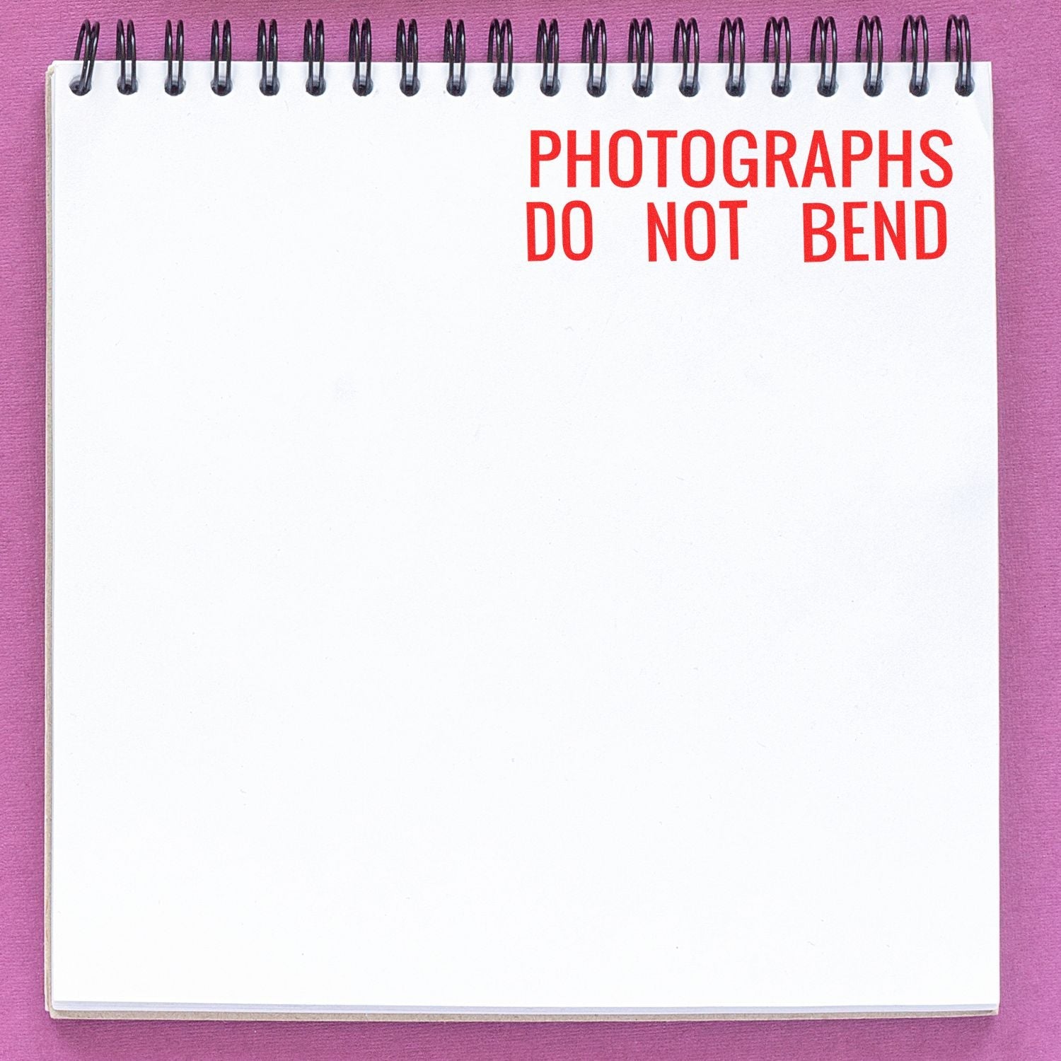 A notebook with PHOTOGRAPHS DO NOT BEND stamped in red using the Self Inking Photographs Do Not Bend Stamp on a purple background.