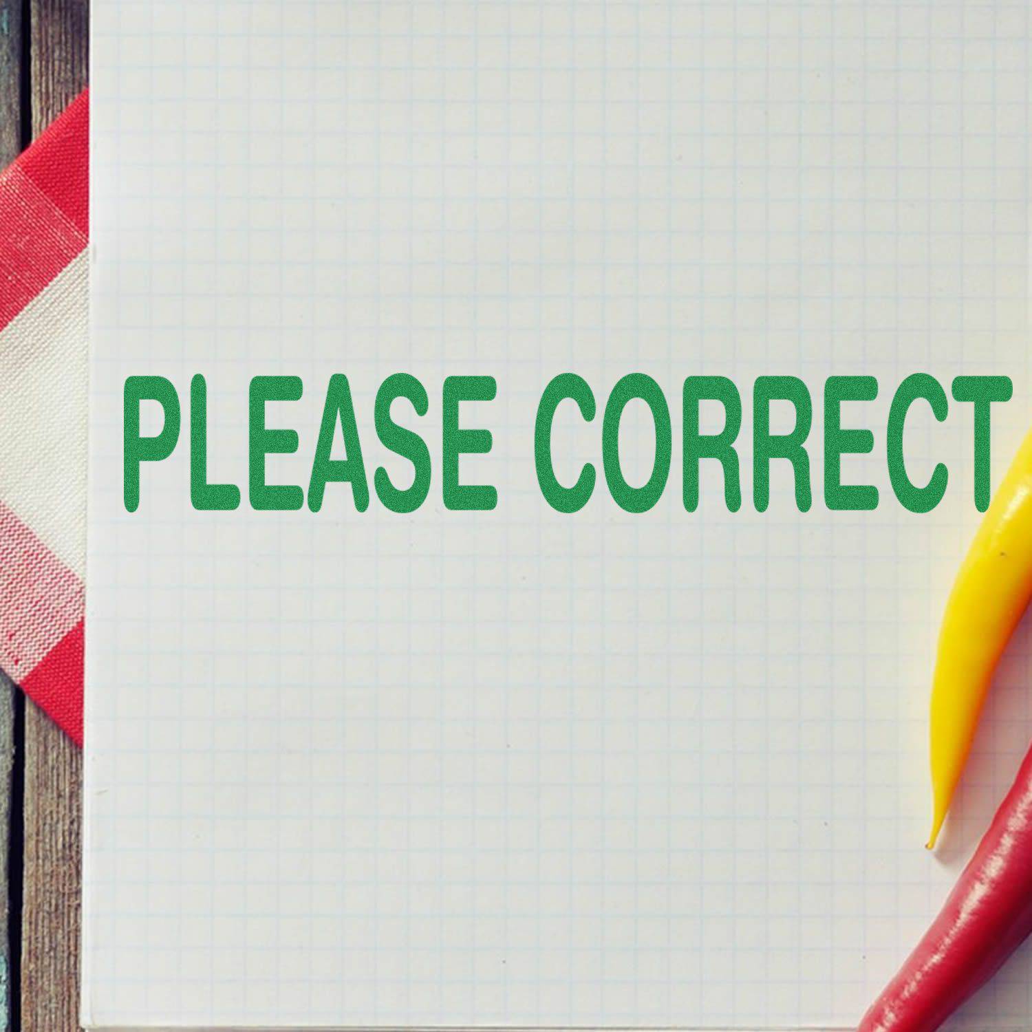 Large Pre-Inked Please Correct Stamp in green ink on graph paper, with a red and white cloth and yellow chili pepper beside it.