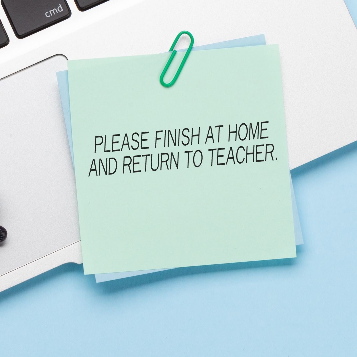 A sticky note with Please Finish At Home and Return To Teacher rubber stamp text is clipped to a laptop keyboard.