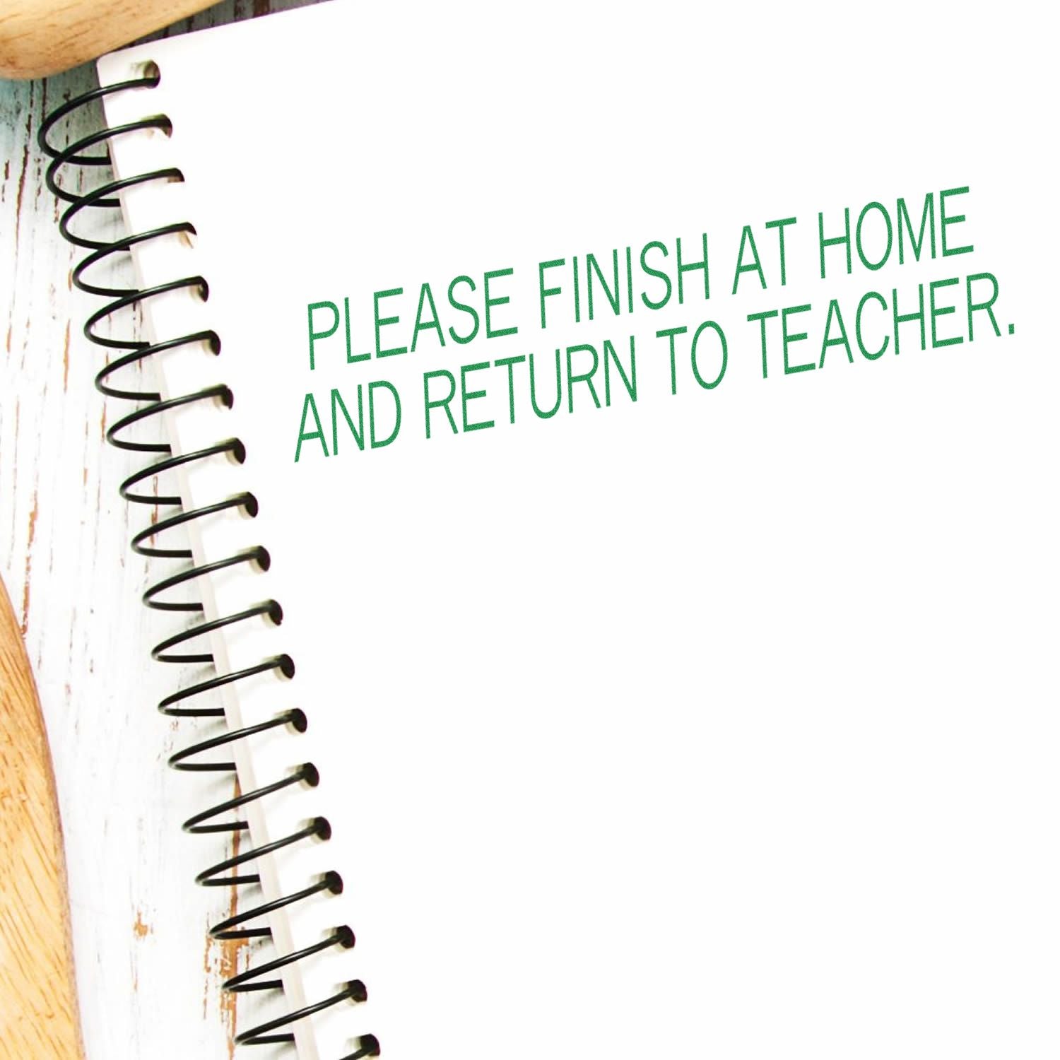 Slim Pre-Inked Please Finish At Home And Return To Teacher Stamp used on a spiral notebook with green ink.