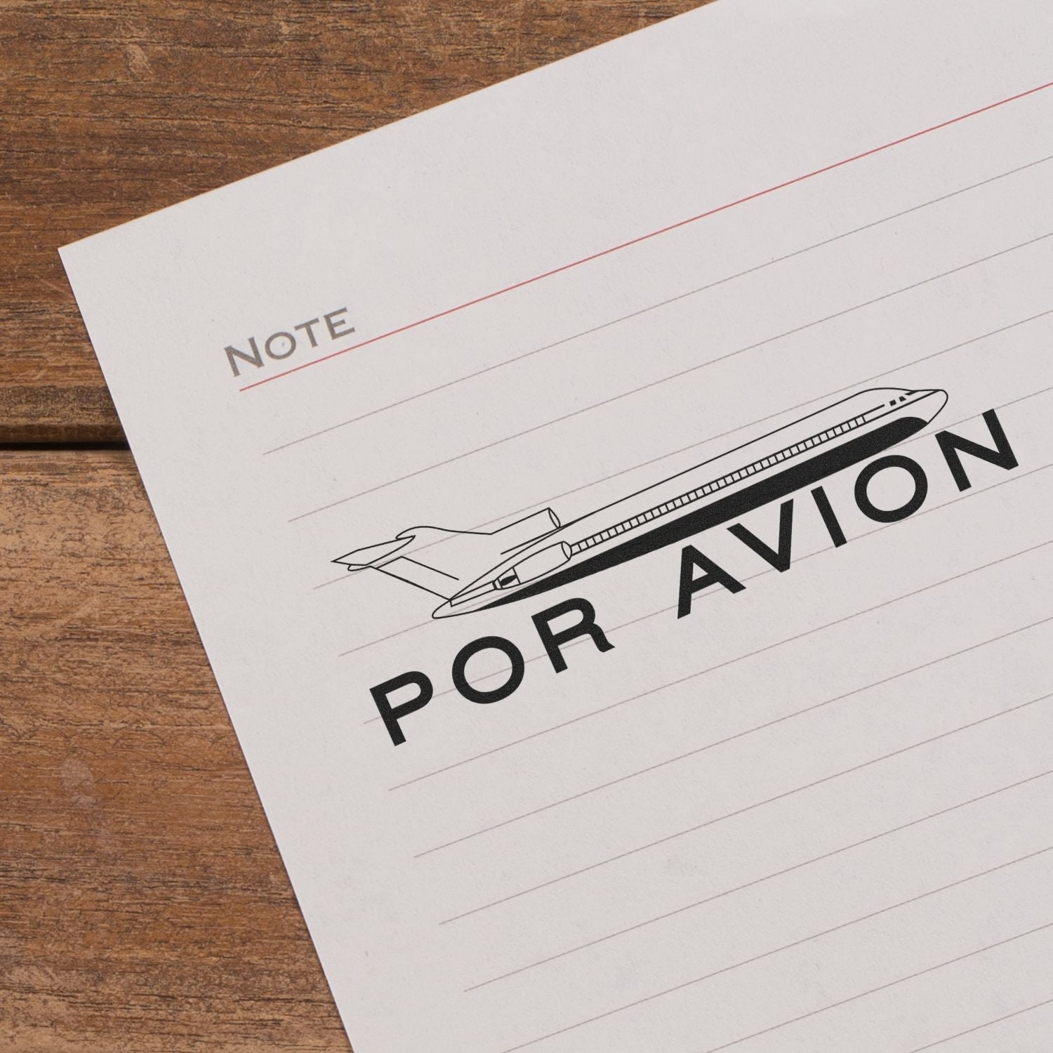 Self Inking Por Avion Stamp on lined paper with an airplane graphic, placed on a wooden surface.