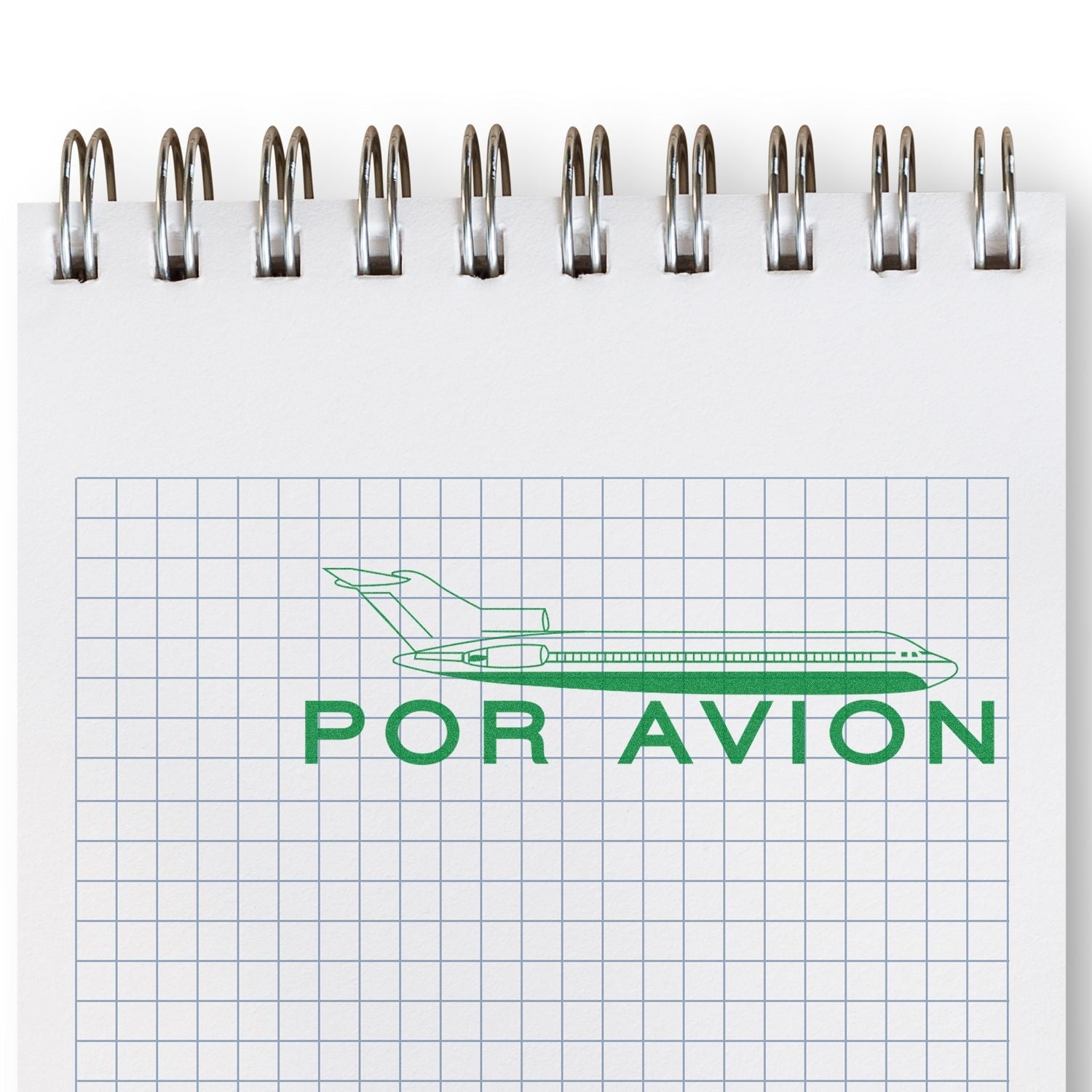 Self Inking Por Avion Stamp imprint on a spiral notebook with graph paper, showing a green airplane and the text POR AVION .