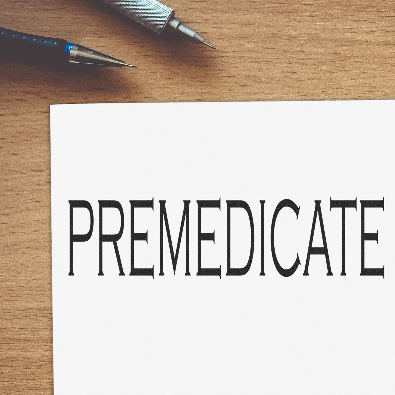 Large Self Inking Premedicate Stamp in use, stamping the word PREMEDICATE on white paper, with a pen nearby on a wooden surface.