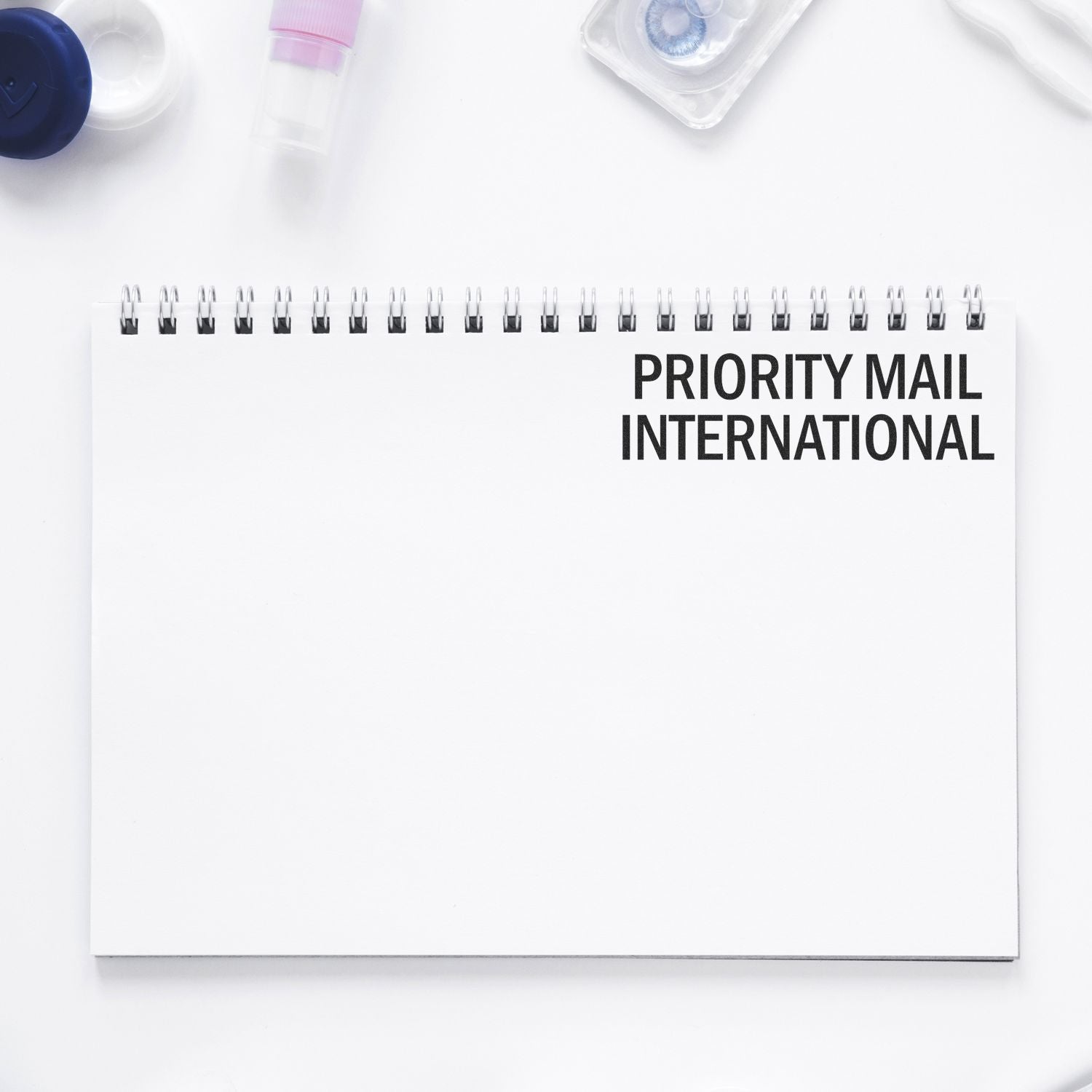 Slim Pre-Inked Priority Mail International Stamp on a white spiral notebook with office supplies around.