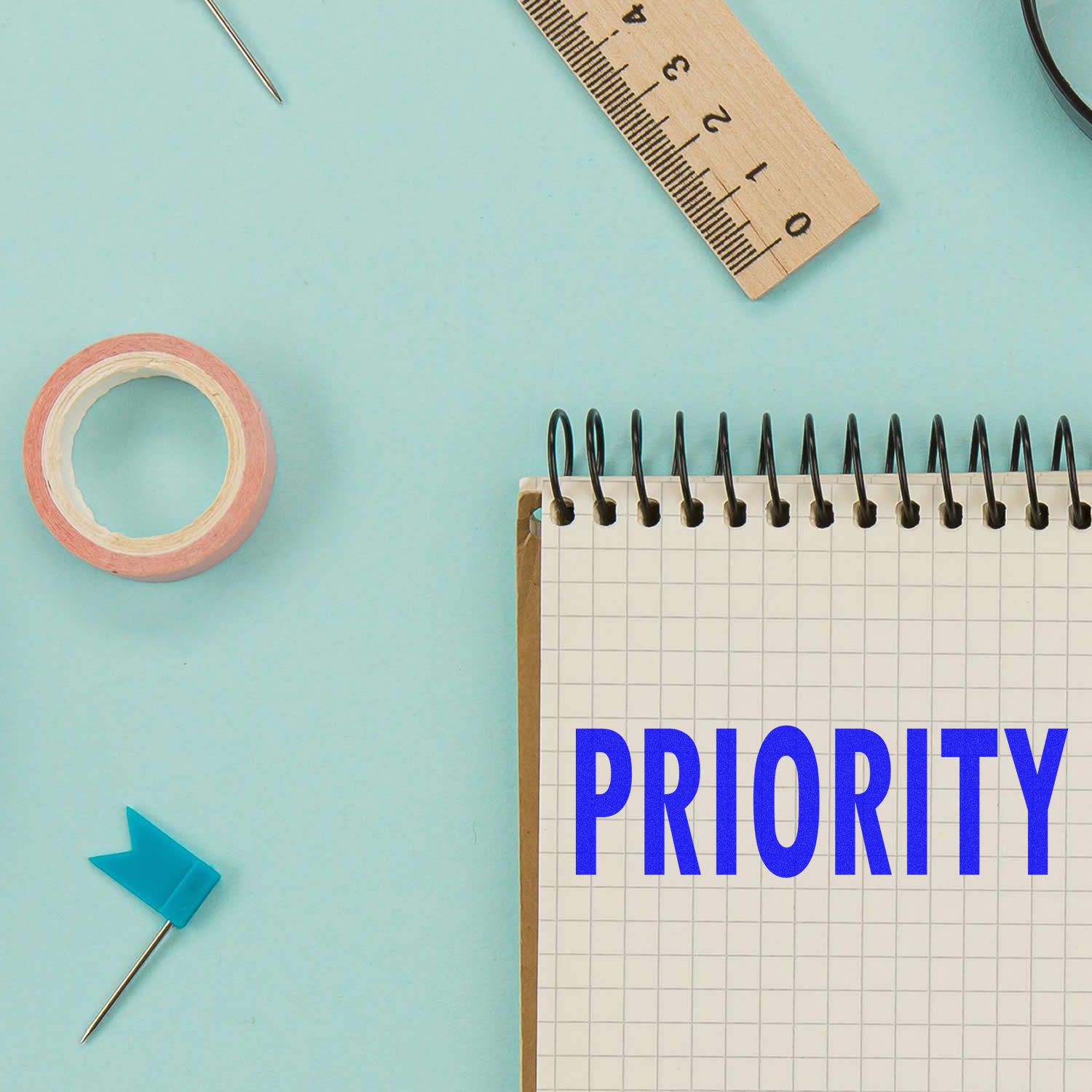 A Large Self Inking Priority Stamp is used on a notebook with the word PRIORITY in blue, surrounded by office supplies on a light blue background.