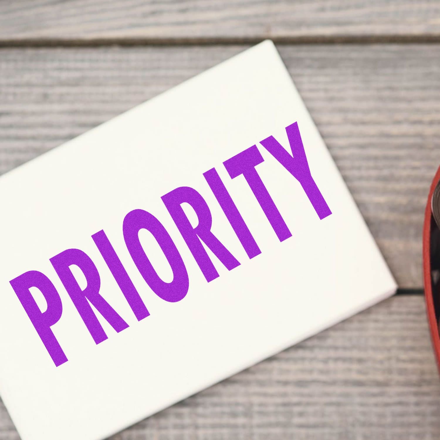 Large Self Inking Priority Stamp in use, stamping the word PRIORITY in bold purple letters on a white package on a wooden surface.