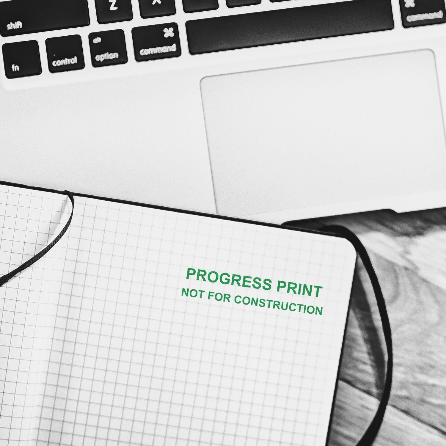 Self Inking Progress Print Stamp marking PROGRESS PRINT NOT FOR CONSTRUCTION in green ink on a grid notebook, next to a laptop.