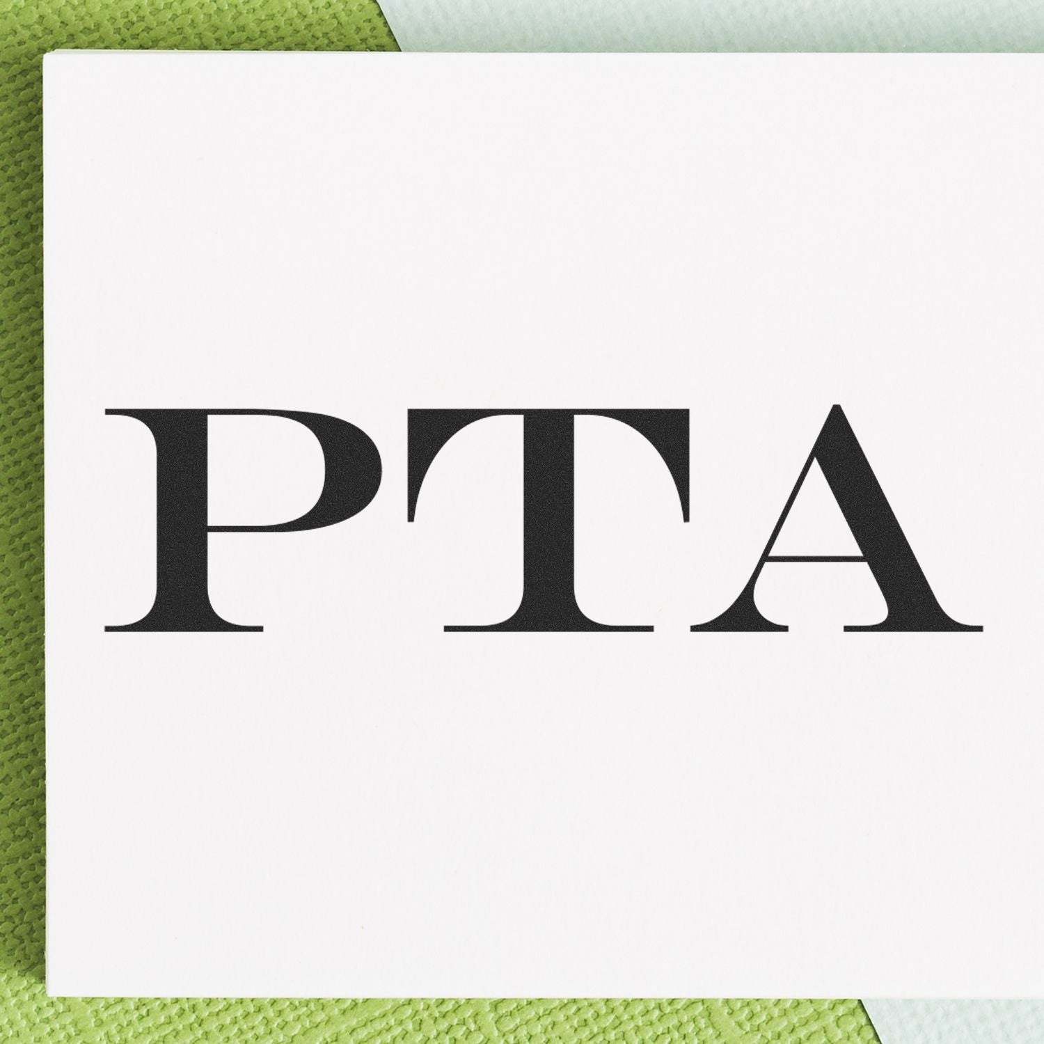 PTA Rubber Stamp in use, displaying bold 'PTA' text on white paper, placed on a textured green and white background.