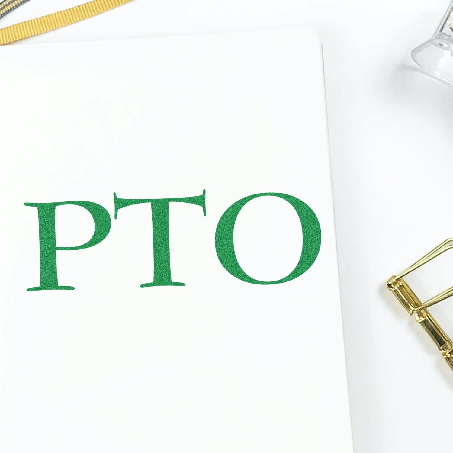 Green PTO rubber stamp mark on white paper with a gold pen clip and a clear stamp holder in the background.