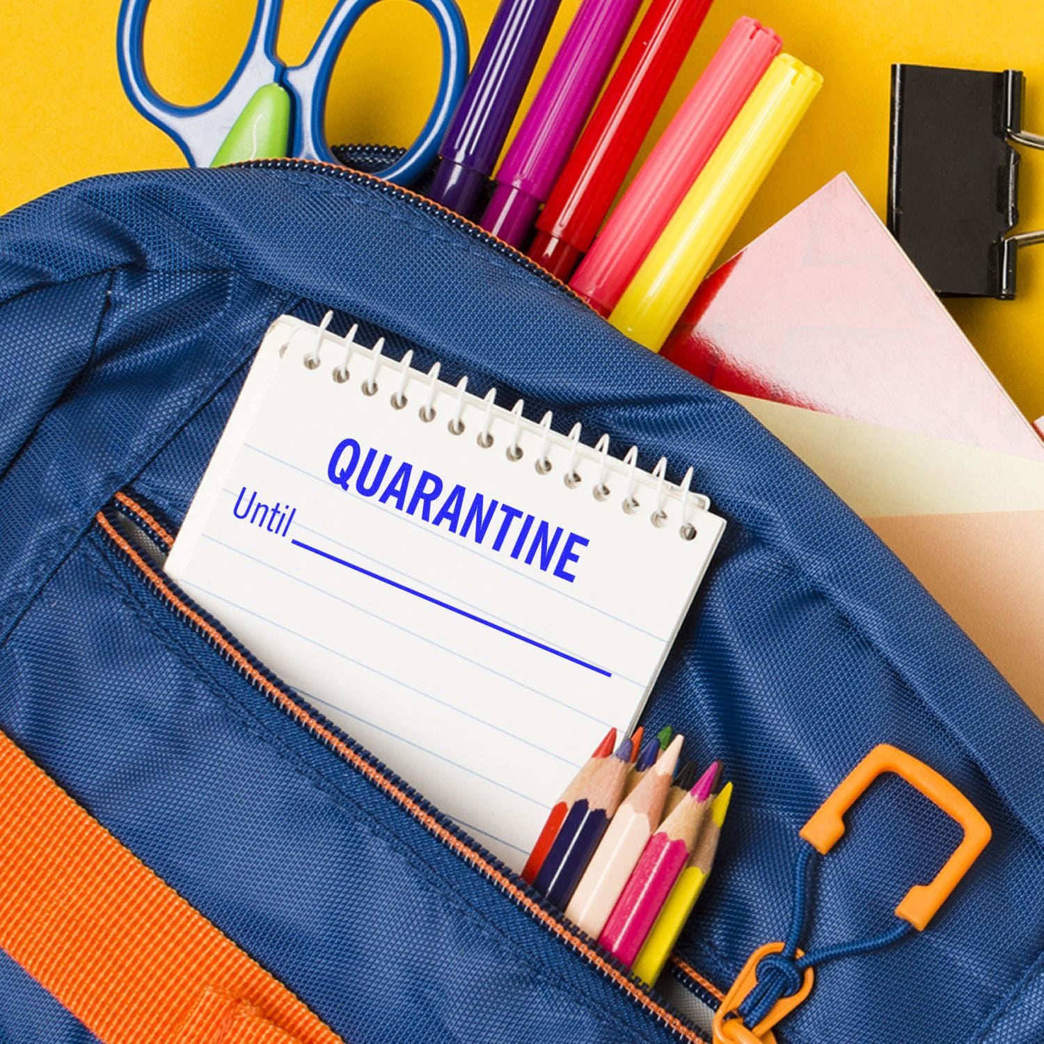 A Large Quarantine Until Rubber Stamp is shown on a notepad inside a blue backpack, surrounded by colorful pens, pencils, and scissors.