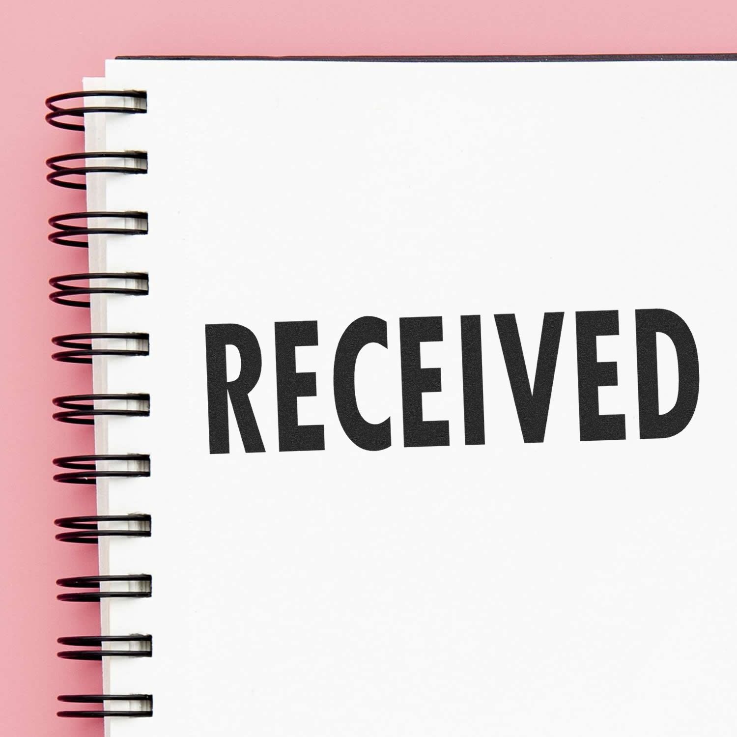 Slim Pre-Inked Received Stamp marking RECEIVED in bold black letters on a white spiral notebook against a pink background.