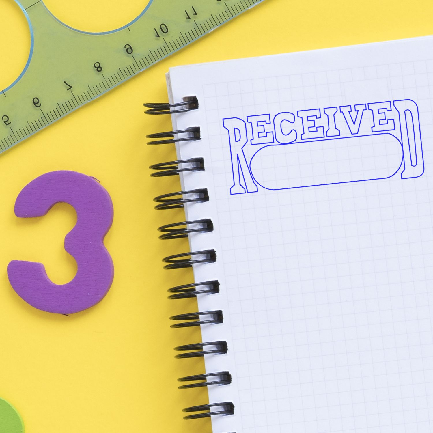 Self Inking Received with Date Box Stamp in use on a notebook, with a ruler and number 3 on a yellow background.