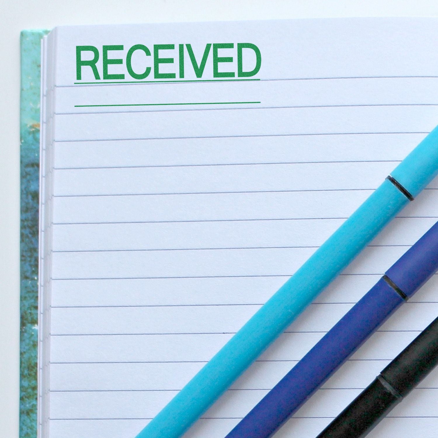 Notebook with 'Received with Line Rubber Stamp' in green ink at the top, next to three colored pens.