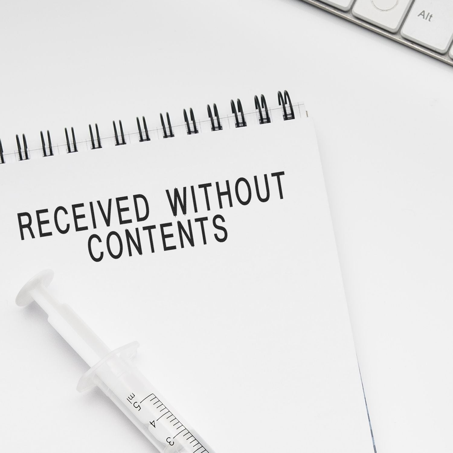 A notebook stamped with Received Without Contents in bold letters, next to a syringe and a keyboard on a white desk.