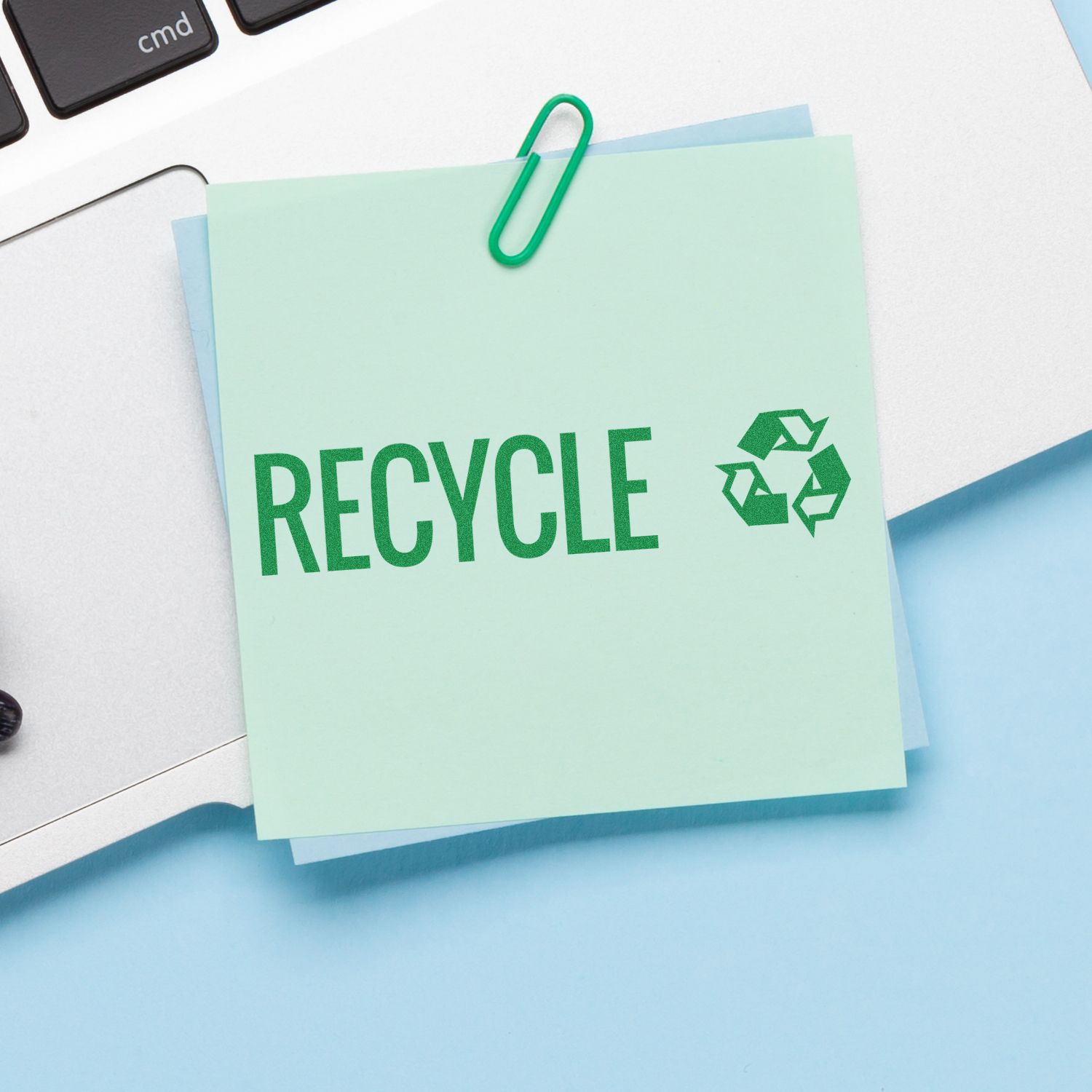 Recycle with Logo Rubber Stamp on a green sticky note clipped to a laptop keyboard, featuring the recycle symbol.