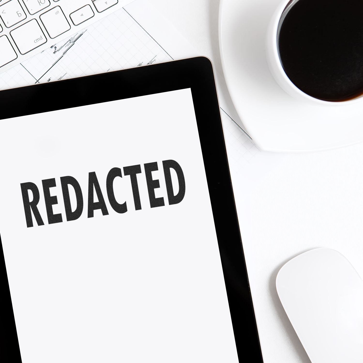 Slim Pre-Inked Redacted Stamp on a document beside a tablet, keyboard, coffee cup, and mouse on a white desk.