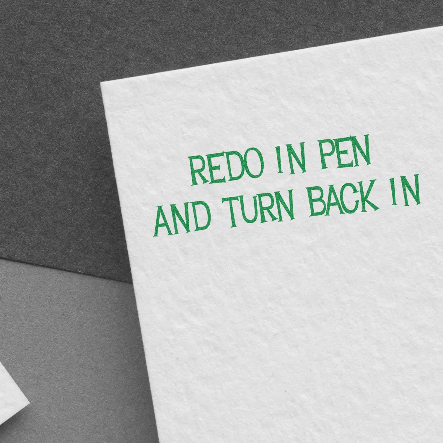 White paper with green 'Redo In Pen And Turn Back In' rubber stamp text on a gray background.