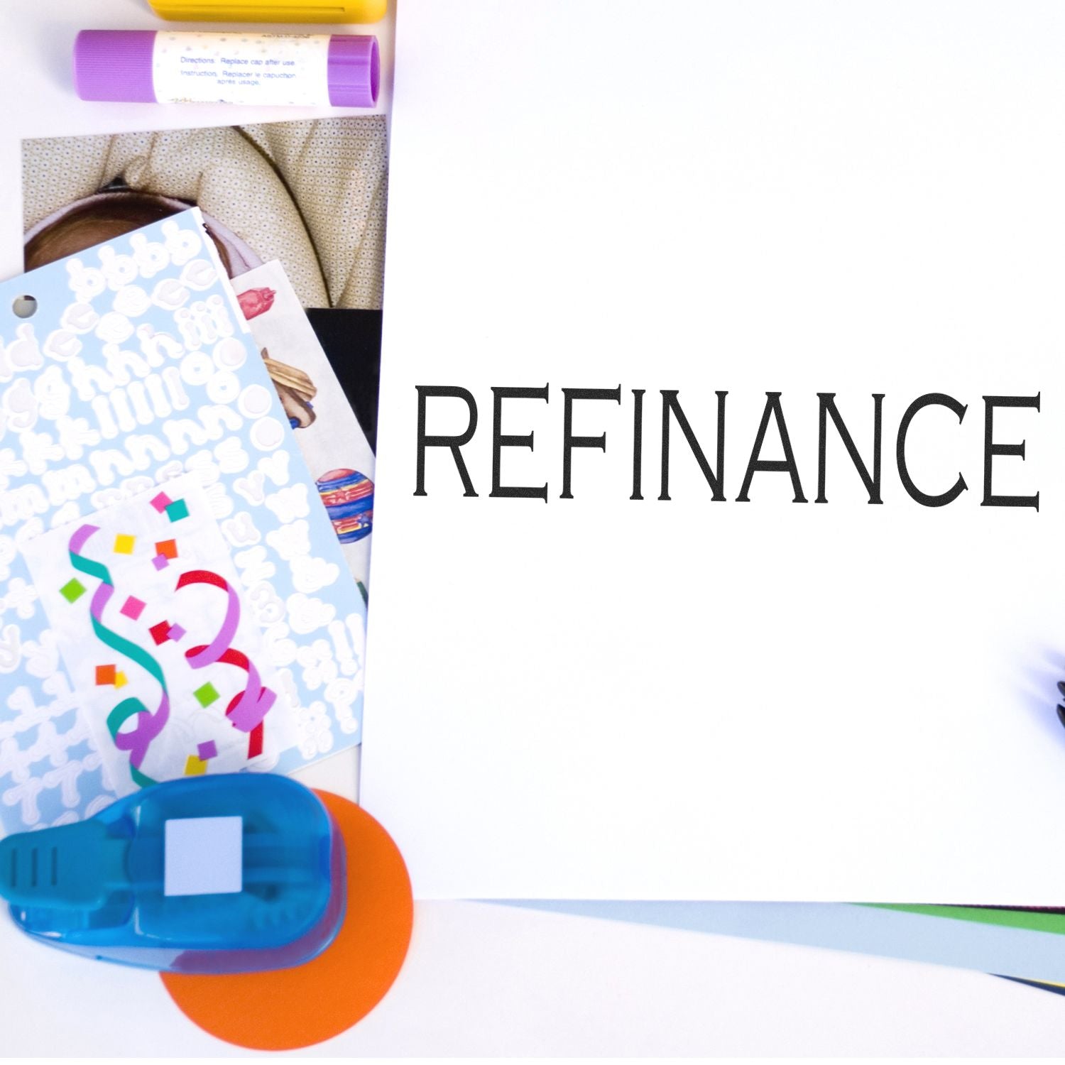 Large Refinance Rubber Stamp used on a white paper, surrounded by colorful office supplies including stickers, a glue stick, and a hole puncher.