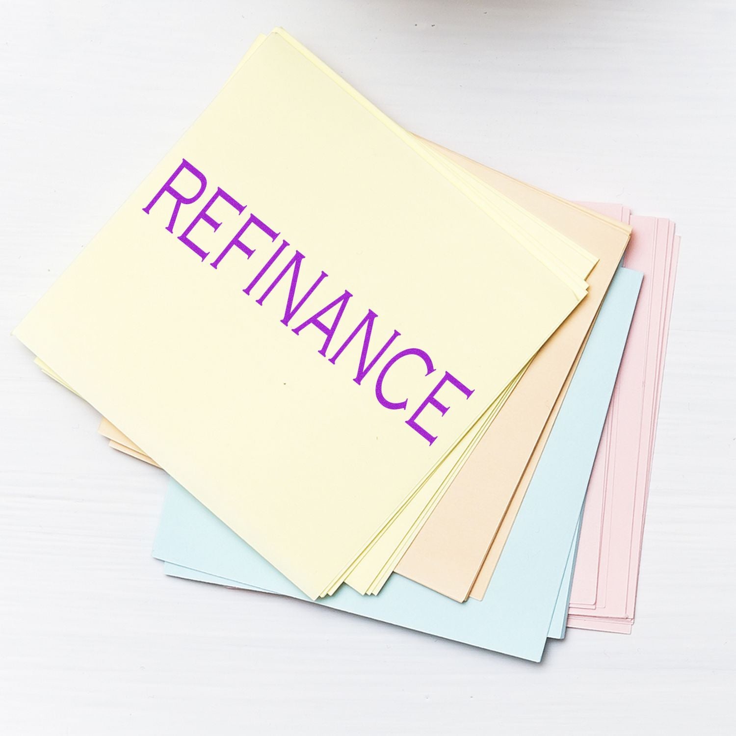 Stack of pastel papers stamped with 'Refinance' in purple ink using a Refinance rubber stamp.