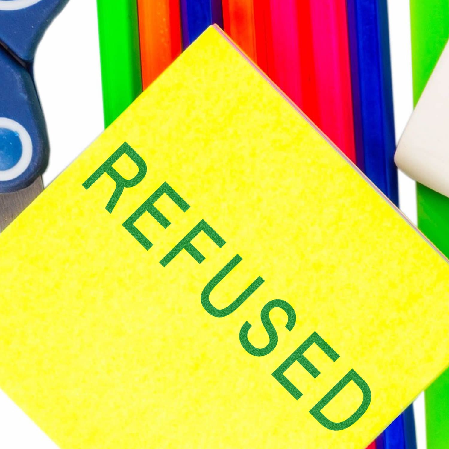 Yellow paper with REFUSED stamped in green ink, surrounded by colorful pens and scissors. Focus word: Refused Rubber Stamp.