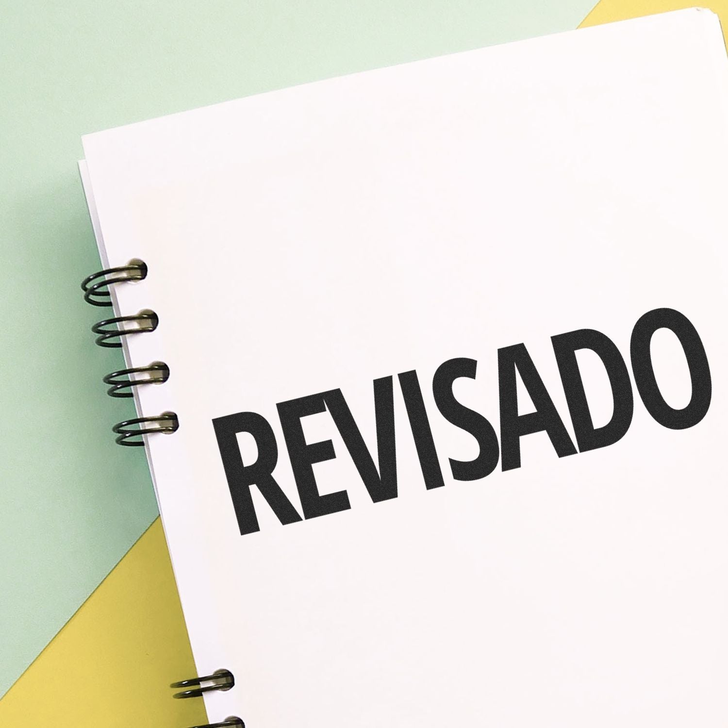 Notebook with 'Revisado' rubber stamp on the cover, placed on a pastel-colored background.