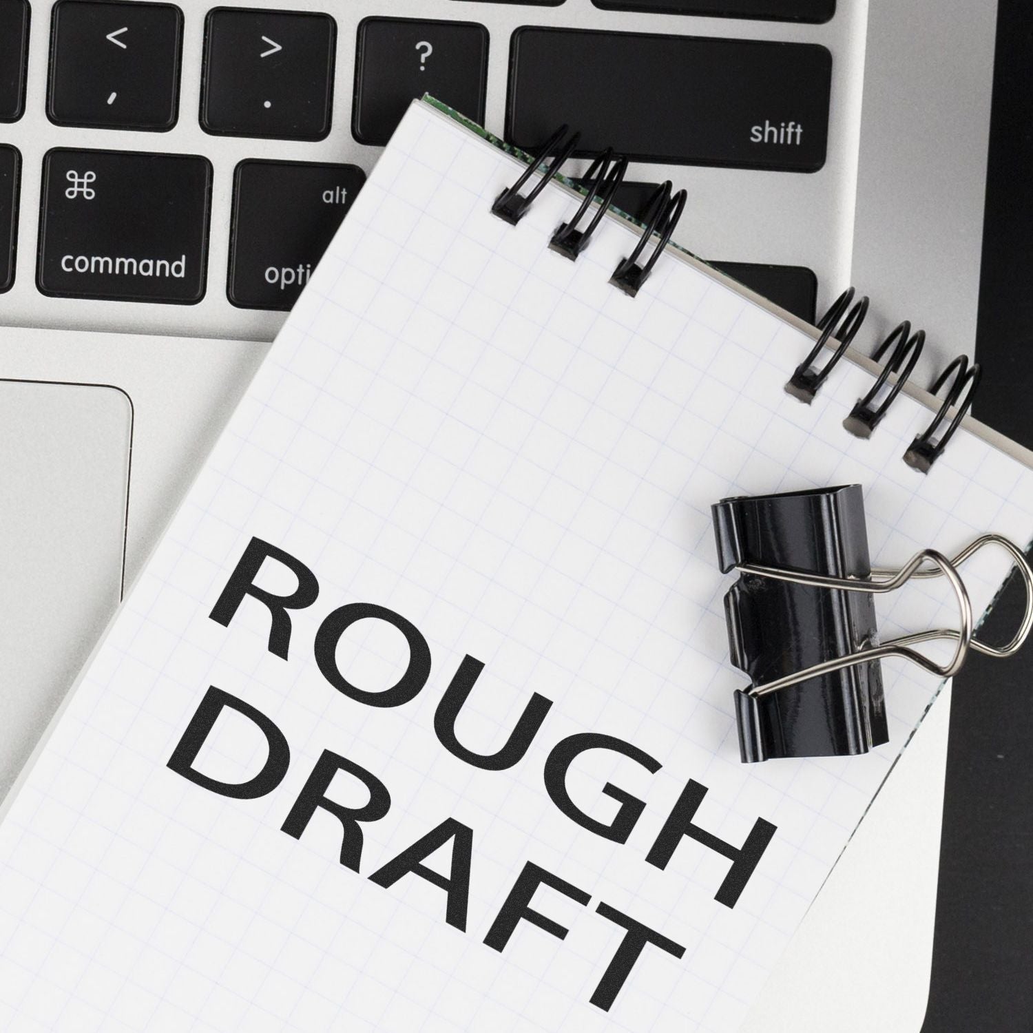 A Self Inking Rough Draft Stamp is used on a notepad labeled Rough Draft, placed on a laptop keyboard with a black binder clip.