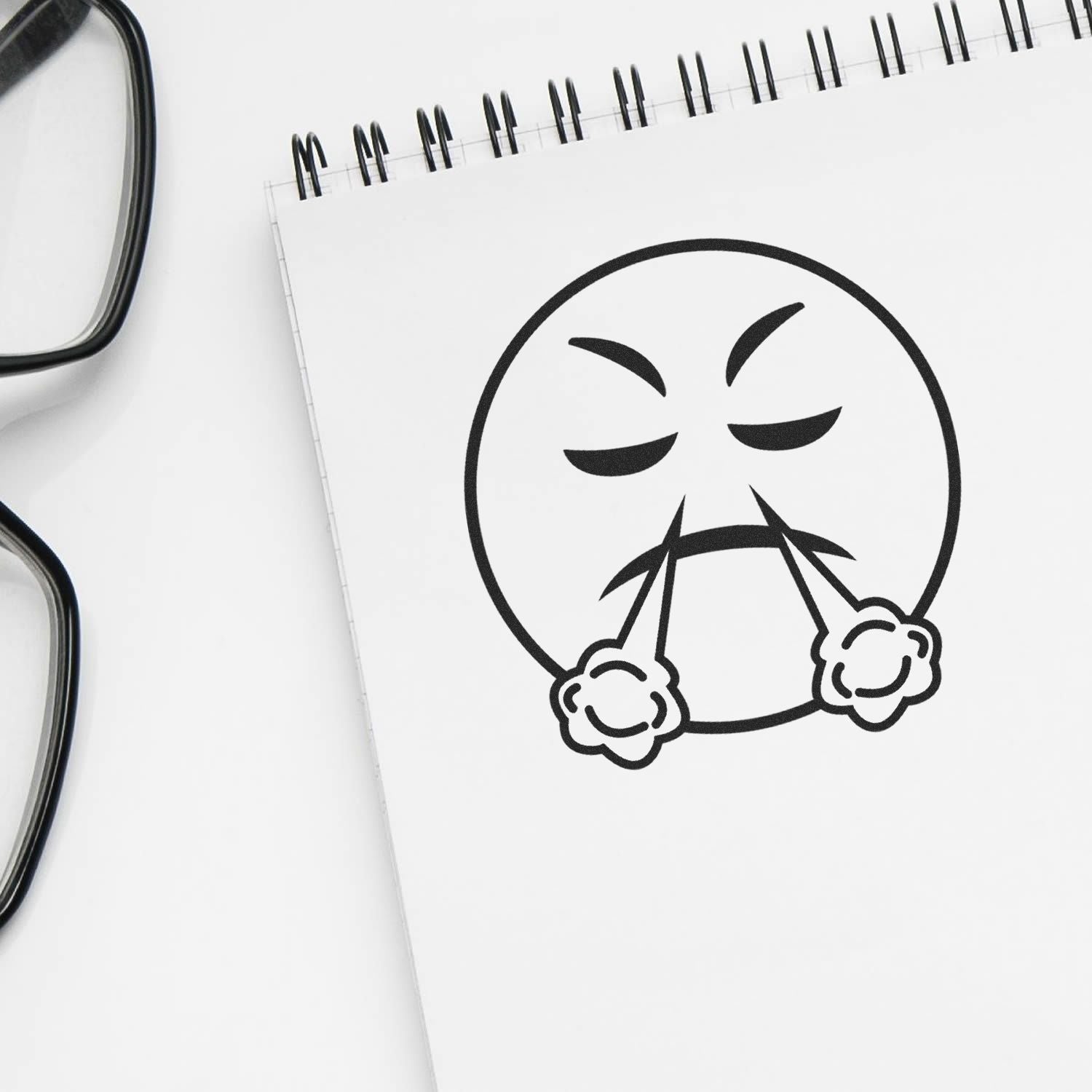 Round Angry Smiley Rubber Stamp on a white notepad with glasses beside it. The stamp shows an angry face with steam coming out.