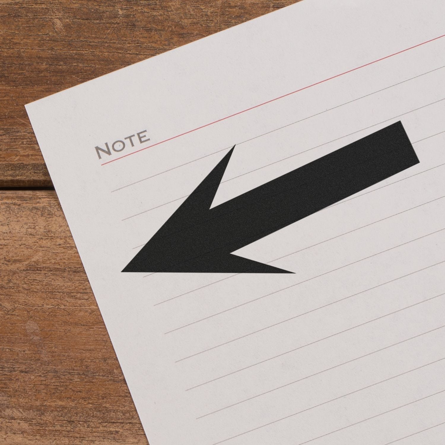 Self Inking Round Arrow Stamp in use, creating a bold black arrow on a lined notebook page labeled Note on a wooden surface.