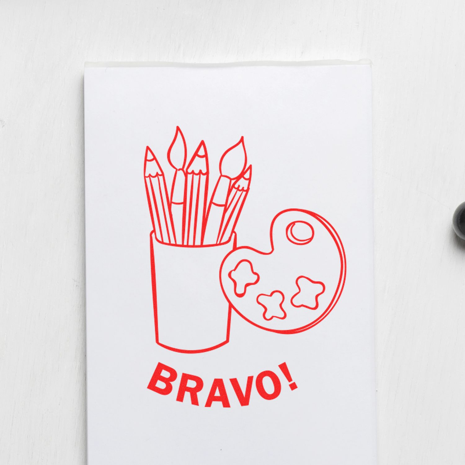 Self Inking Round Bravo Stamp imprint showing red art supplies and palette with the word BRAVO! on white paper.