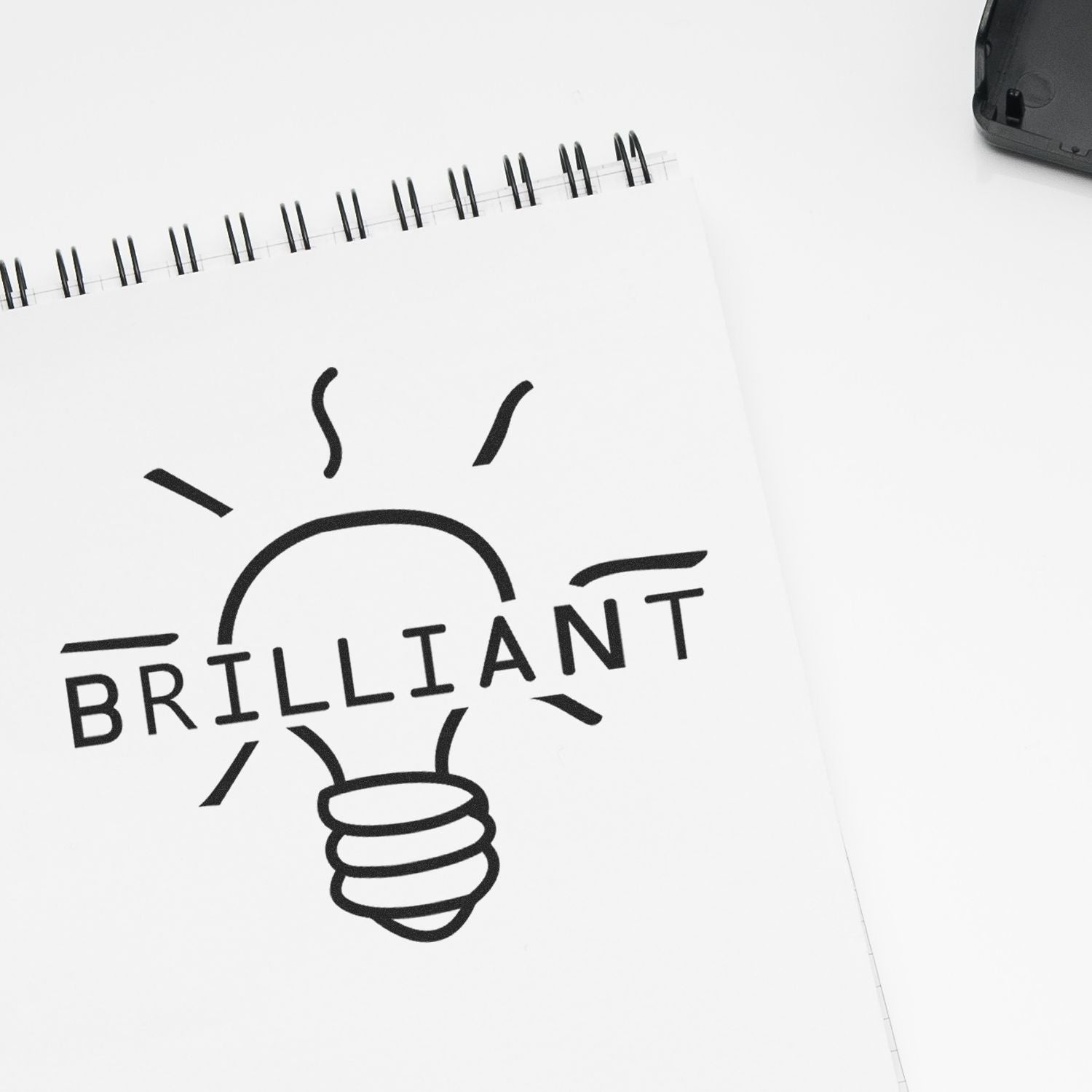 Self Inking Round Brilliant Stamp used on a white notepad, creating a light bulb design with the word BRILLIANT in bold letters.