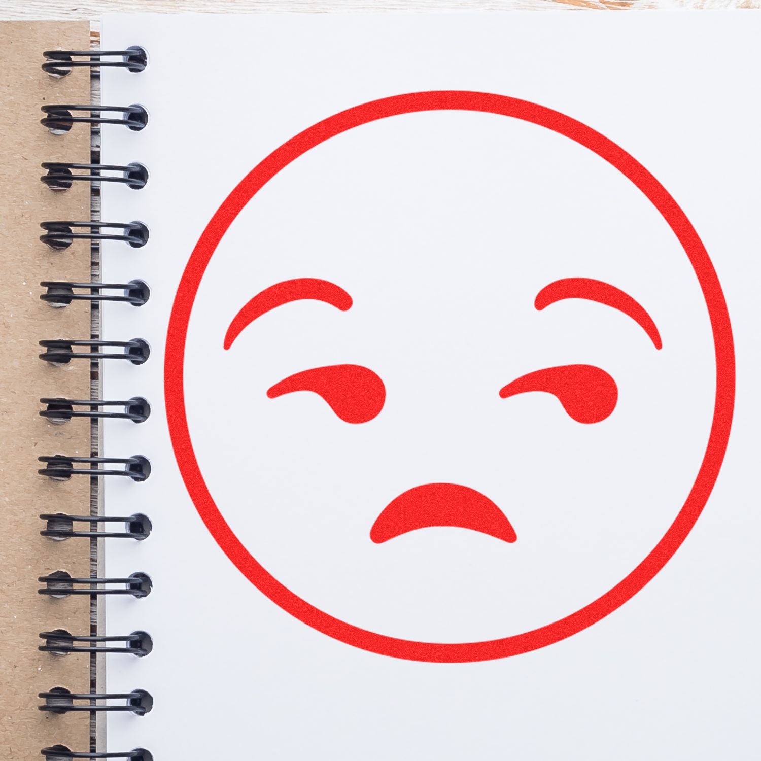 Self Inking Round Calm Smiley Stamp in red ink on a white spiral notebook, displaying a calm, relaxed facial expression.