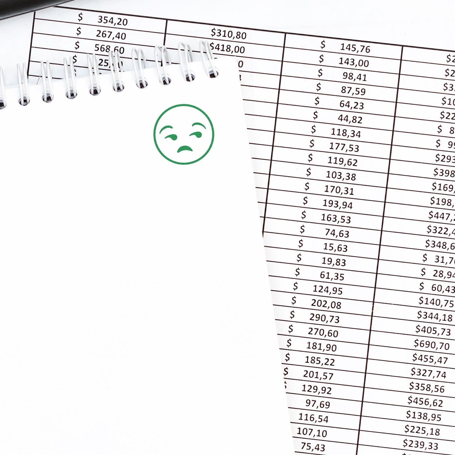 Round calm smiley rubber stamp on a white notepad next to a financial spreadsheet with various amounts listed.