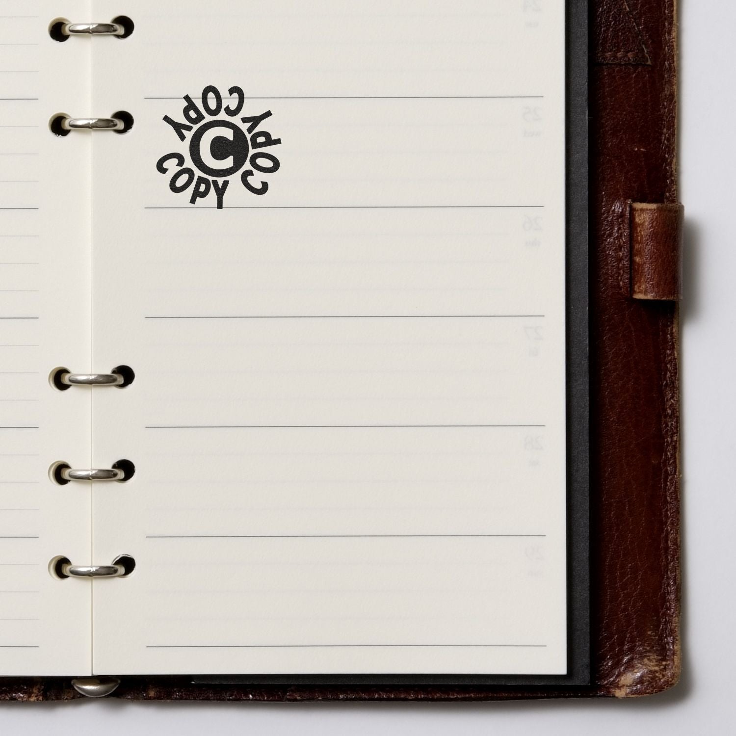 Open planner with a Round Copy Copy Copy Rubber Stamp impression on a blank page, next to a brown leather cover.