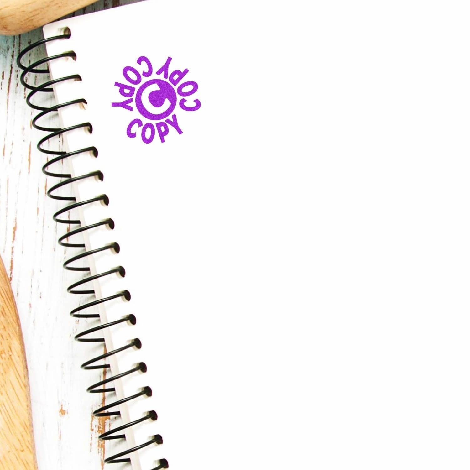 Self Inking Round Copy Copy Copy Stamp imprint in purple ink on a white spiral notebook, placed on a white wooden surface.