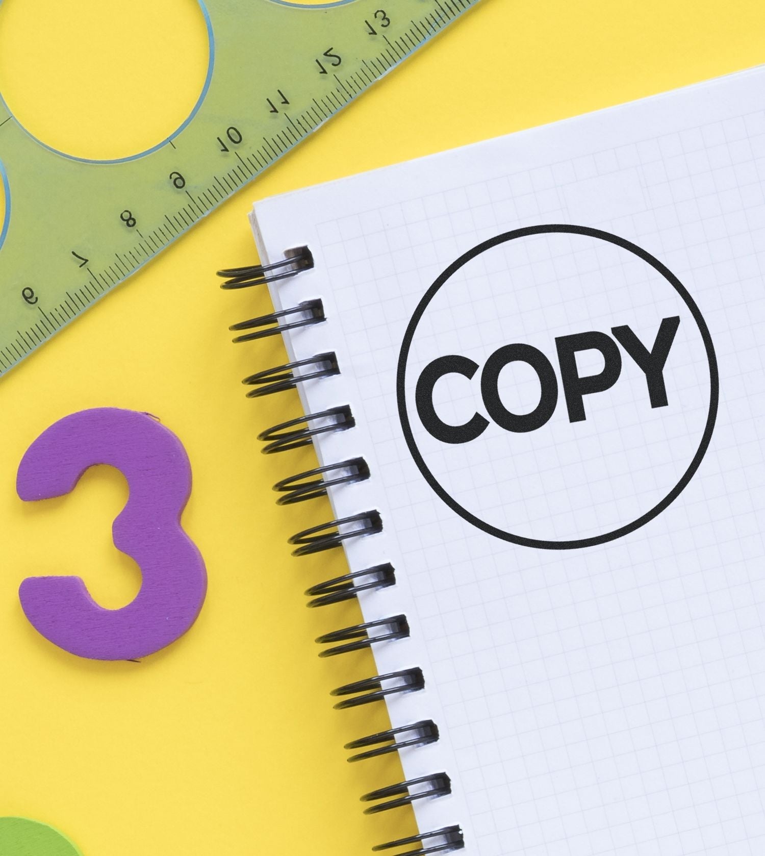 Self Inking Round Copy Stamp marking COPY on a spiral notebook, with a ruler and number 3 on a yellow background.