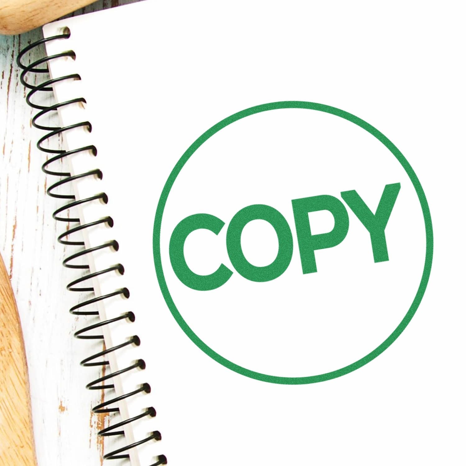 Self Inking Round Copy Stamp imprint in green ink on a white spiral notebook, placed on a wooden surface.