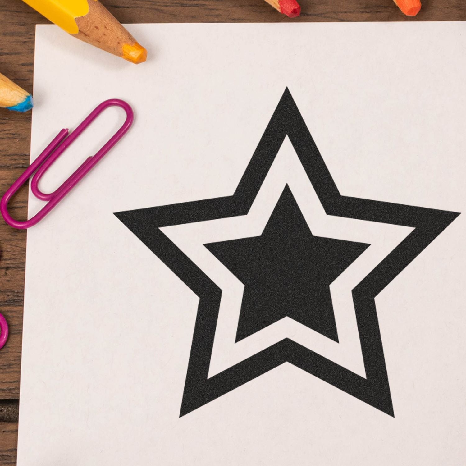 Round Double Star Rubber Stamp design on white paper, surrounded by colored pencils and a pink paperclip on a wooden surface.