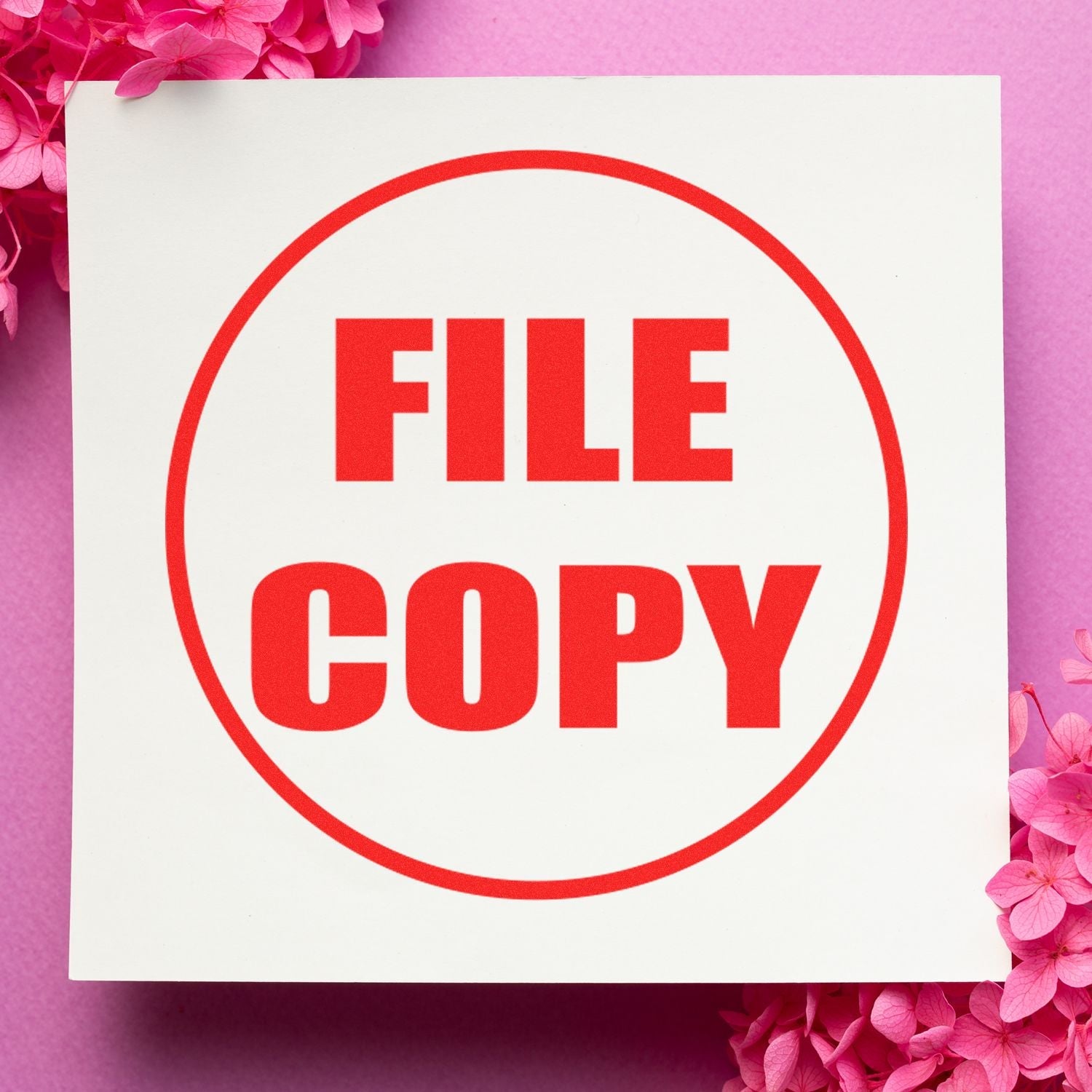 Self Inking Round Draft Stamp imprint with FILE COPY in red on white paper, surrounded by pink flowers on a pink background.