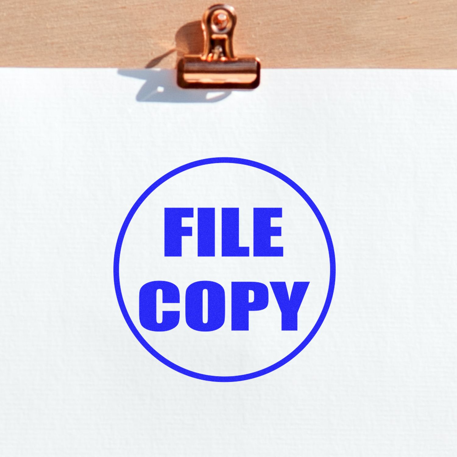 A document stamped with FILE COPY in blue ink using the Self Inking Round File Copy Stamp, clipped to a wooden board.