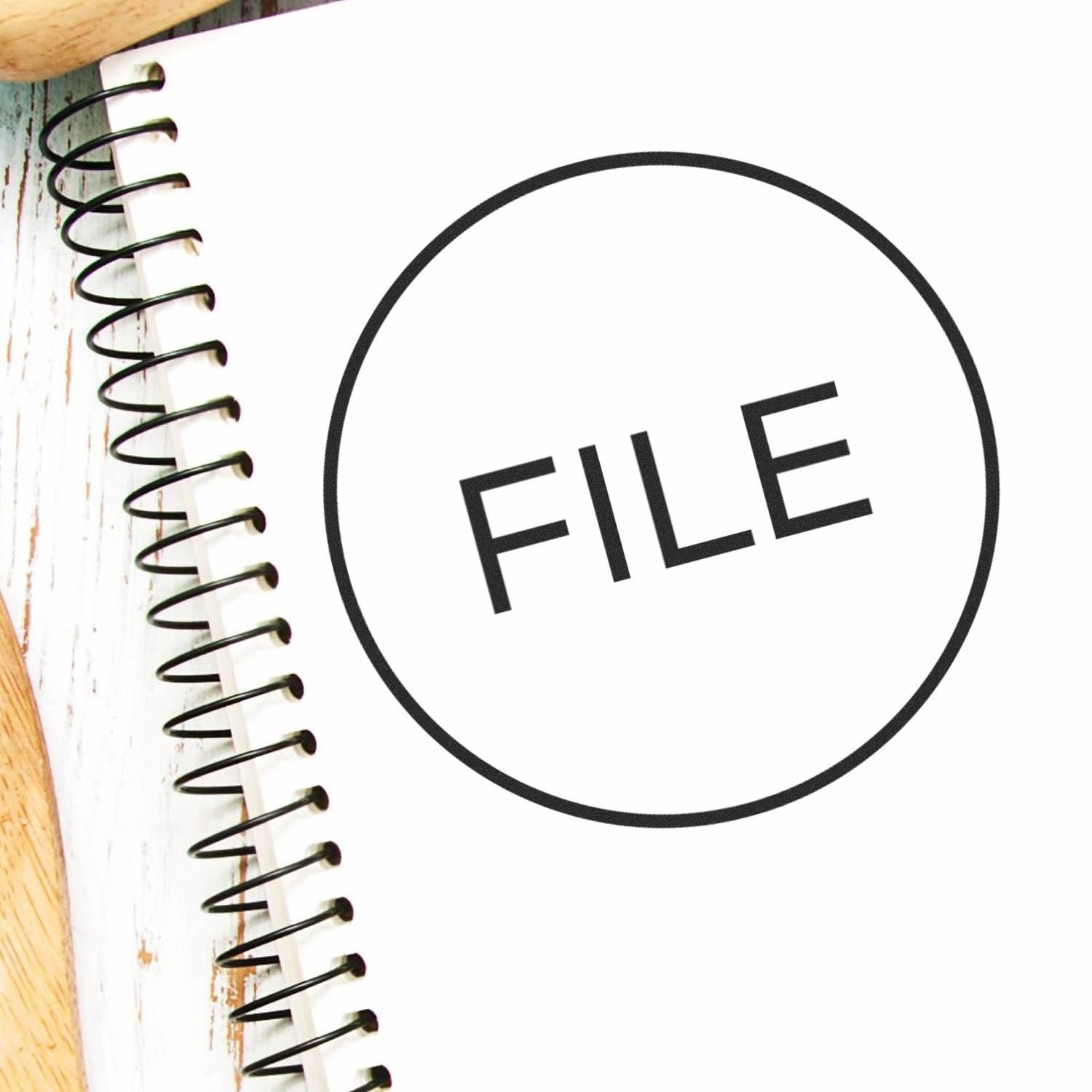 Self Inking Round File Stamp marking the word FILE on a white spiral notebook, placed on a wooden surface.