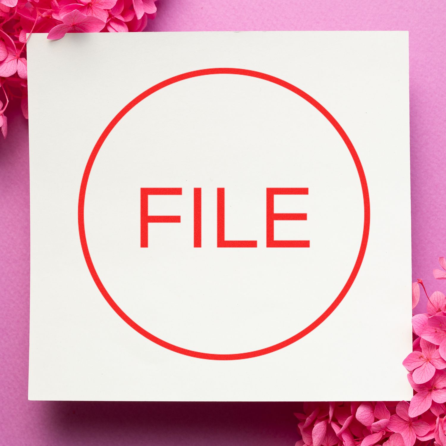 Self Inking Round File Stamp in use, showing a red FILE text within a circle on white paper, surrounded by pink flowers on a pink background.