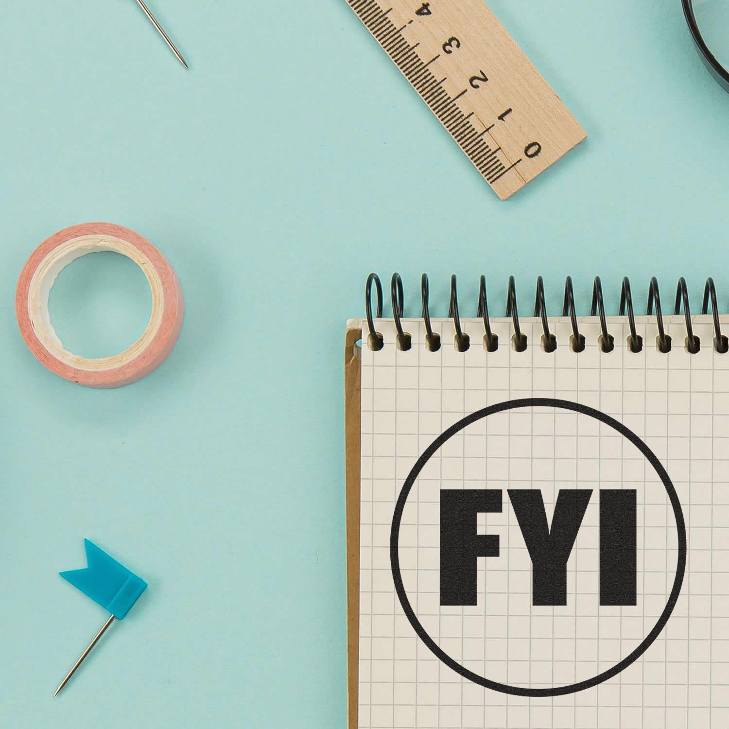 Round FYI rubber stamp on a spiral notebook, surrounded by a ruler, tape, and a blue flag pin on a light blue background.